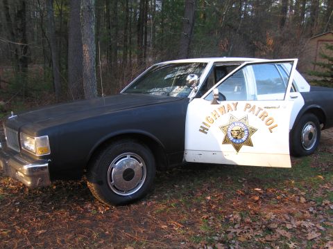 1991 Ford LTD Crown Victoria - This police car, possibly a 1991 Ford Crown Victoria LTD, is seen parked outdoors with its driver's side door open.