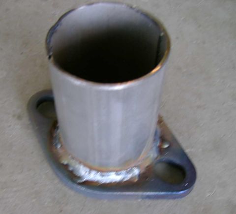 1994 Mazda MX-3 - Close-up of a metal exhaust pipe flange, showing weld marks and bolt holes on a concrete surface.