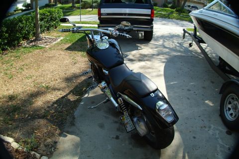 1995 Ford Bronco - A black motorcycle is parked in front of a black Ford Bronco and a boat on a trailer, with a residential street in the background.