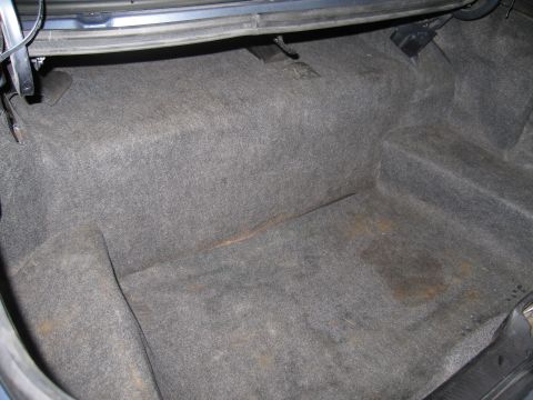 1991 Ford LTD Crown Victoria - The interior of a car's trunk is shown, gray carpeting with visible stains.
