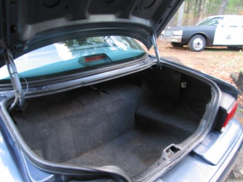 1991 Ford LTD Crown Victoria - The open trunk of a car is shown, with a police car visible in the background.