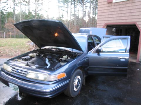 1991 Ford LTD Crown Victoria - A blue 1991 Ford Crown Victoria LTD is parked with its hood and driver's door open, revealing the engine compartment.