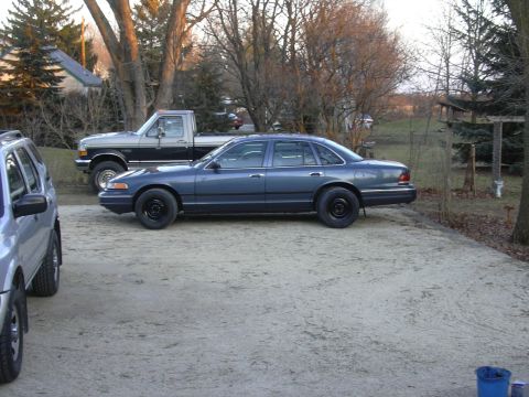 1996 Ford Crown Victoria - A 1996 Ford Crown Victoria sedan is seen parked in a lot next to a pickup truck and another vehicle.