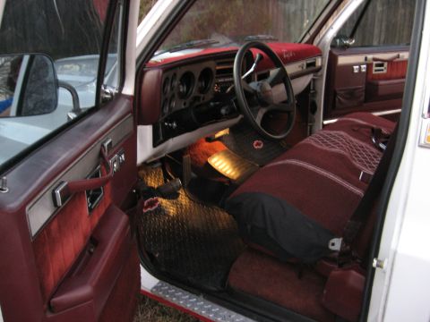 1979 Ford Bronco - The interior of a white truck features maroon seats, door panels, and dashboard accents, with a view of the steering wheel and pedals.