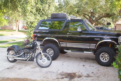 1995 Ford Bronco - A black Ford Bronco and a custom motorcycle are parked side-by-side in a driveway.
