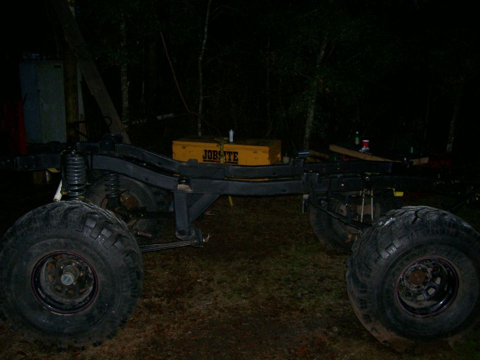 Truck frame with large tires and a yellow toolbox on top, viewed from the side at night