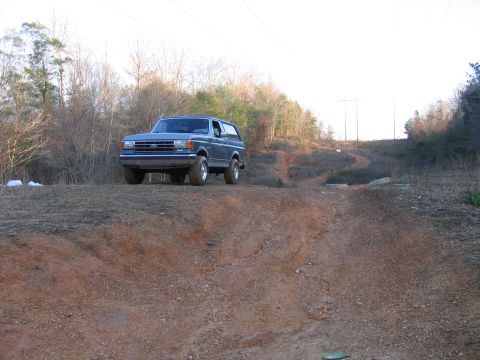 1989 Ford Bronco - 1989 Ford Bronco parked on a dirt road with trees in the background.