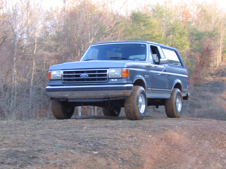 Blue Ford Bronco parked on a dirt hill with trees in the background