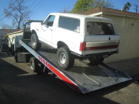 1990 Ford Bronco - A white Ford Bronco is being towed on a flatbed truck.
