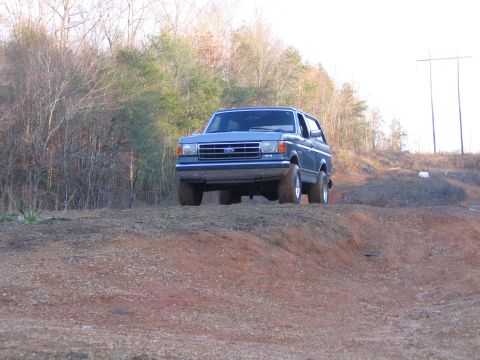 1989 Ford Bronco - A blue Ford Bronco navigates a dirt incline, showing its front grille and side profile.