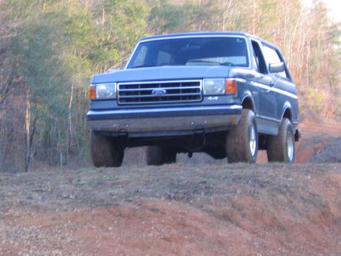 1989 Ford Bronco - This blue 1989 Ford Bronco 4x4 is captured driving on a dirt path surrounded by trees.