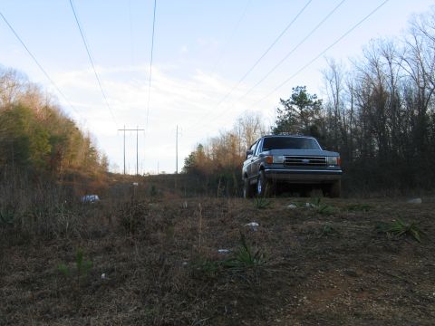 1989 Ford Bronco - A gray Ford Bronco is parked on a dirt incline under a sky with power lines stretching across it.