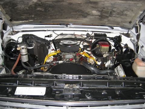 1979 Ford Bronco - Engine bay of a white vehicle, showing a V8 engine with an aftermarket air filter and yellow spark plug wires.