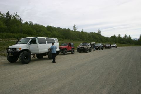 2003 Jeep TJ - A group of modified off-road vehicles are lined up on a gravel road in a wooded area.