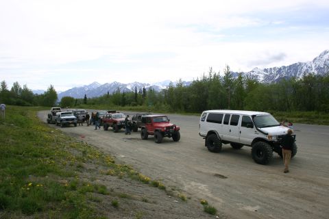 2003 Jeep TJ - A group of off-road vehicles, including a white van and several Jeeps, are gathered on a dirt road with a mountainous backdrop.