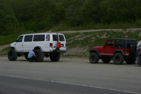 2003 Jeep TJ - A red Jeep Wrangler is parked next to a white van with a person working on its tire.