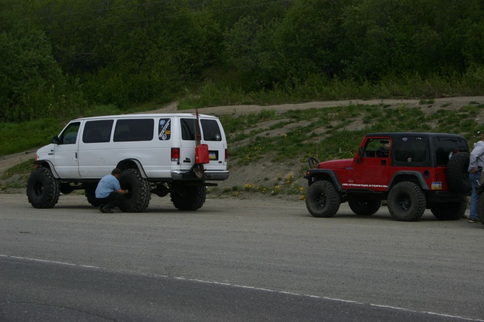 Red Jeep Wrangler with black top and large tires, parked on a dirt road