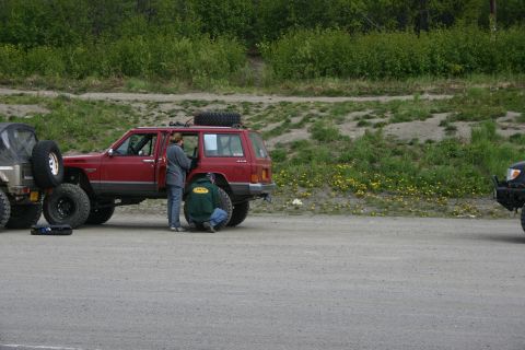2003 Jeep TJ - Two people attend to a red Jeep Cherokee XJ, parked next to other off-road vehicles.