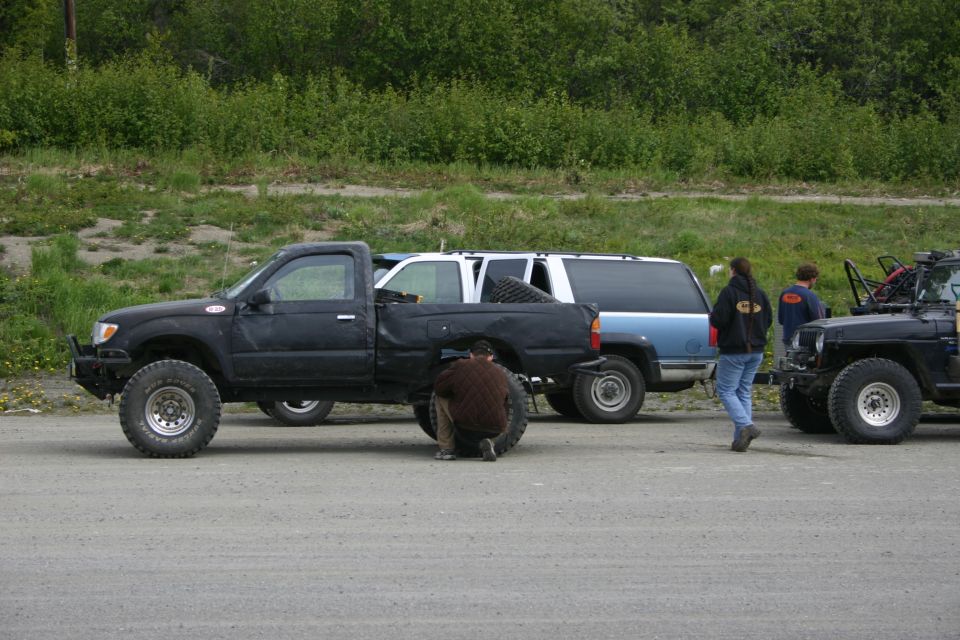 Black pickup truck with lifted suspension, blue SUV, and black Jeep parked on gravel lot