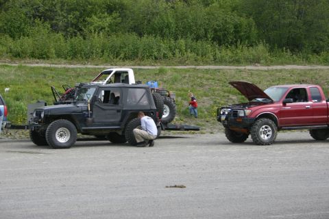 2003 Jeep TJ - A black 2003 Jeep TJ is parked next to a red Toyota pickup truck with its hood open, with a person attending to the Jeep's tire.