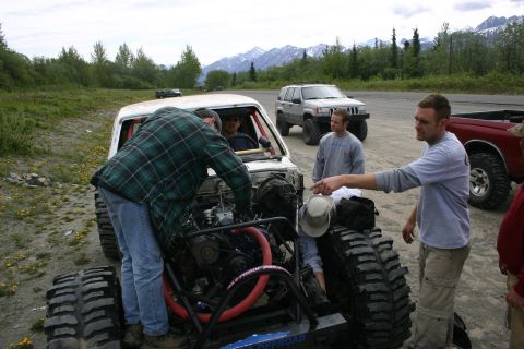 2003 Jeep TJ - Several people gather around a modified off-road vehicle with its engine exposed, with other vehicles visible in the background.