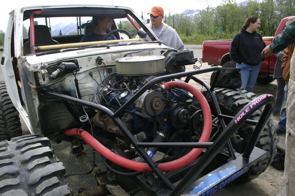 Custom buggy with big tires and exposed engine, people around it