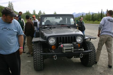 2003 Jeep TJ - A black Jeep Wrangler is parked outdoors with several people around it.