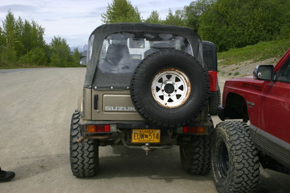 Suzuki Samurai with spare tire on rear door, next to a red Jeep Cherokee