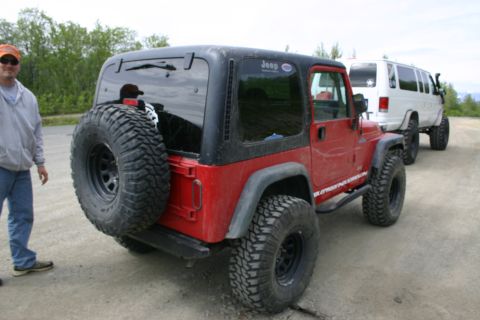 2003 Jeep TJ - A red Jeep Wrangler is parked on a dirt road, with a white van behind it.