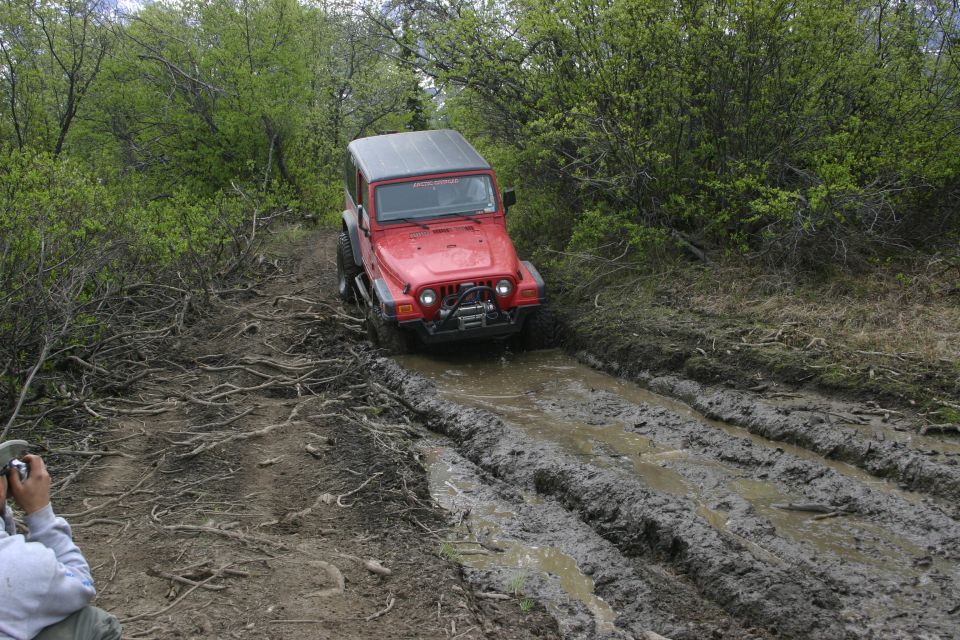 Red 2003 Jeep TJ navigating a muddy trail with exposed roots