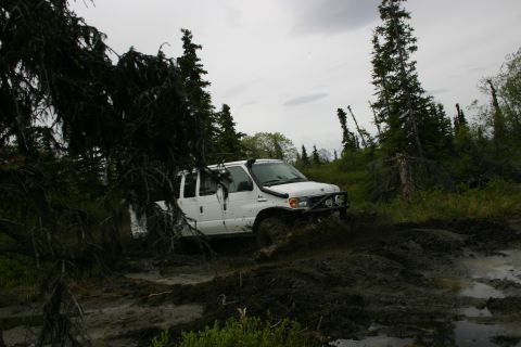2003 Jeep TJ - A white van struggles through a muddy off-road track surrounded by trees.