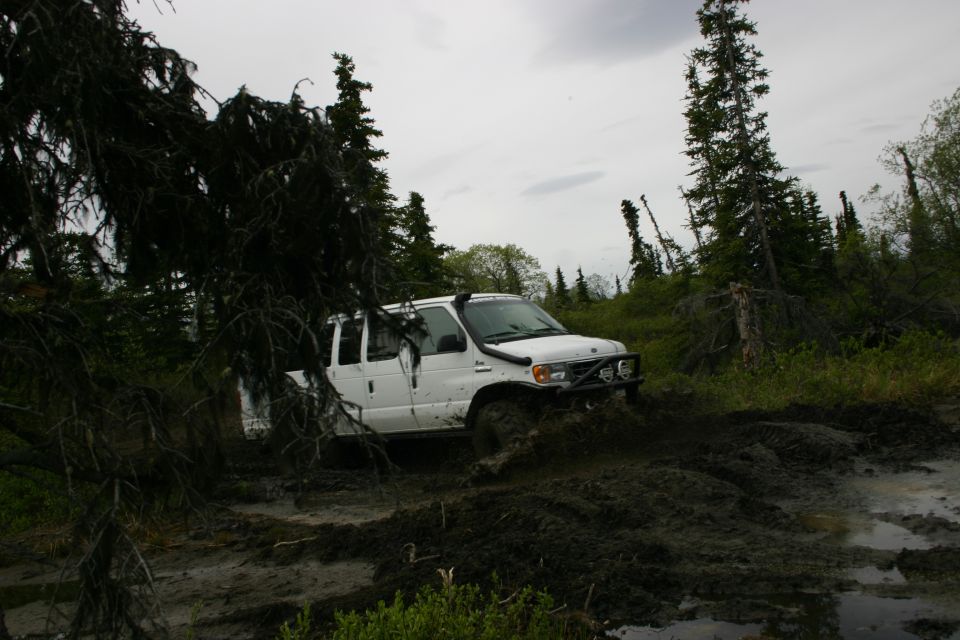 White van navigating a muddy trail in a wooded area