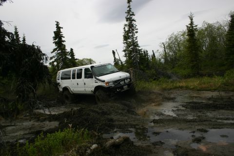 2003 Jeep TJ - A white van navigates a challenging muddy terrain surrounded by trees.