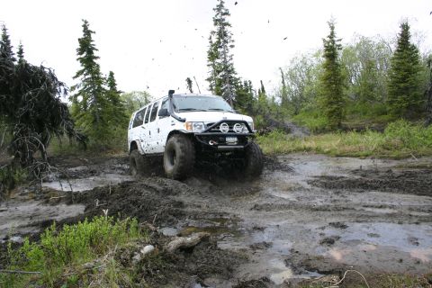2003 Jeep TJ - A white SUV navigates a challenging muddy terrain, kicking up dirt as it goes.