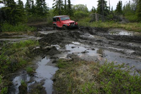 2003 Jeep TJ - A red Jeep Wrangler navigates a muddy trail through a forest.