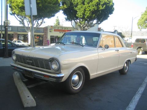 1968 Ford Mustang - This cream-colored 1963 Chevrolet Nova is parked in a lot, with a visible license plate and a glimpse of a pickup truck in the background.