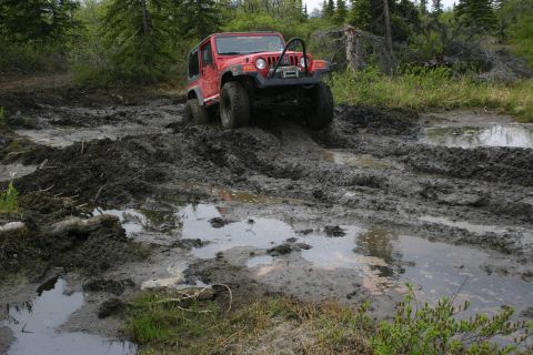 2003 Jeep TJ - A red Jeep Wrangler tackles a challenging muddy off-road course.