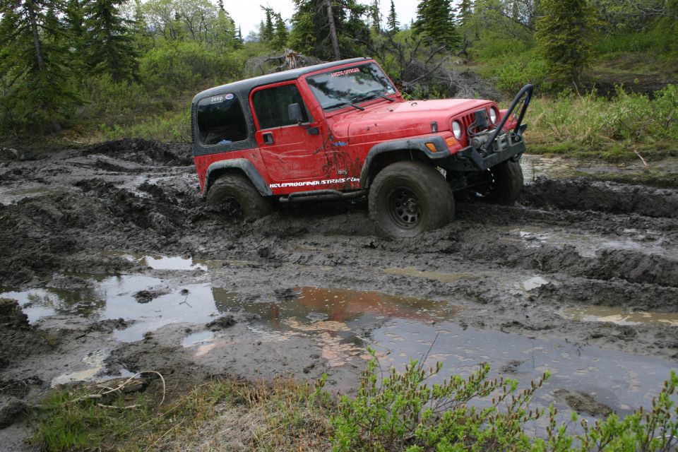 Red 2003 Jeep TJ stuck in deep mud with trees and brush in the background