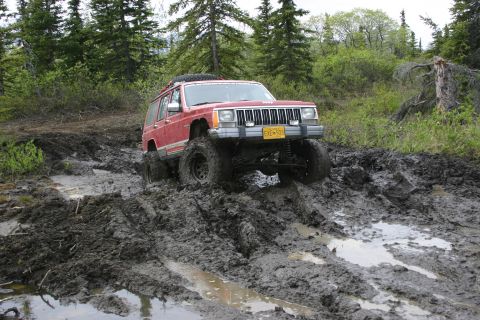 2003 Jeep TJ - A red Jeep Cherokee XJ navigates a muddy trail with large tires.