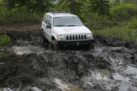 2003 Jeep TJ - A white Jeep Grand Cherokee navigates a challenging muddy off-road path.