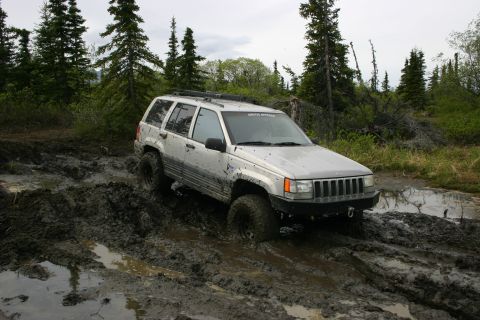 2003 Jeep TJ - A silver Jeep Grand Cherokee navigates a muddy trail, its tires deep in the muck.