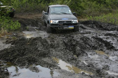 2003 Jeep TJ - This truck is navigating a very muddy off-road trail, with another vehicle visible in the background.