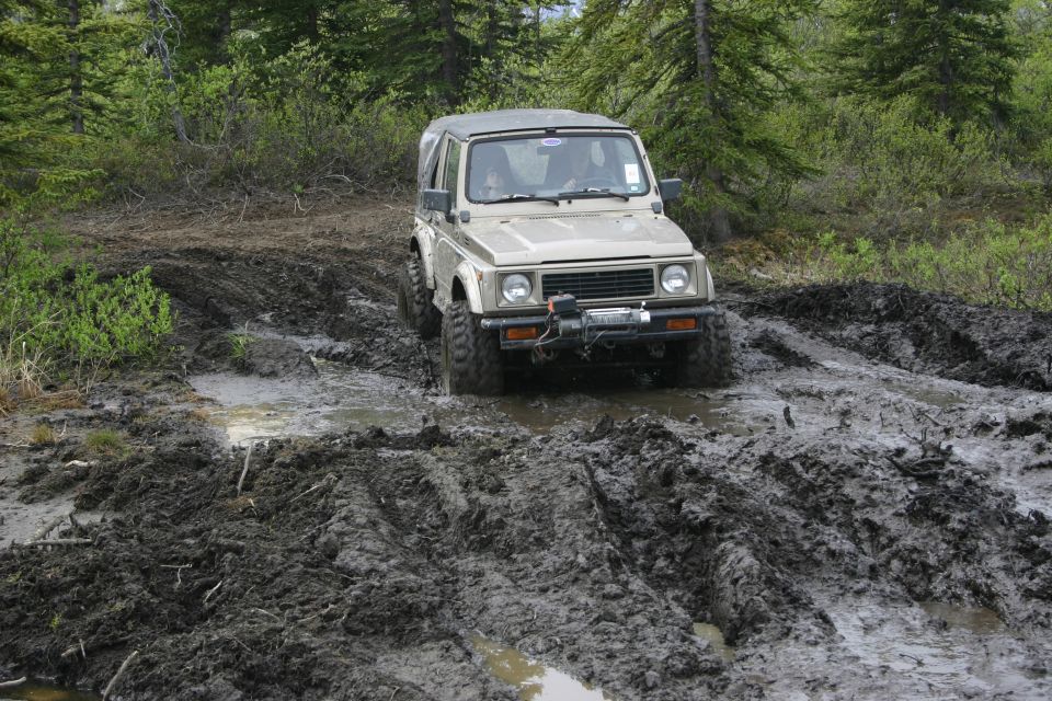 Suzuki Samurai driving through a muddy trail with trees in the background