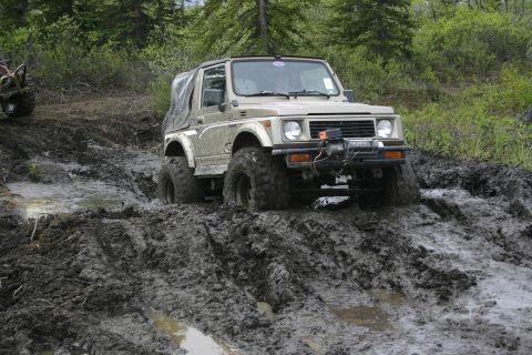 2003 Jeep TJ - An off-road vehicle navigates a challenging muddy terrain, with another vehicle partially visible in the background.