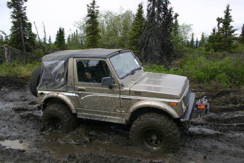 2003 Jeep TJ - This tan soft-top 4x4 appears to be a Suzuki Samurai, not a 2003 Jeep TJ, as it navigates a muddy off-road trail.