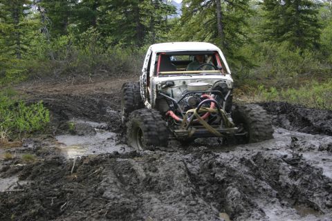 2003 Jeep TJ - This heavily modified off-road vehicle is stuck deep in the mud on a wooded trail.