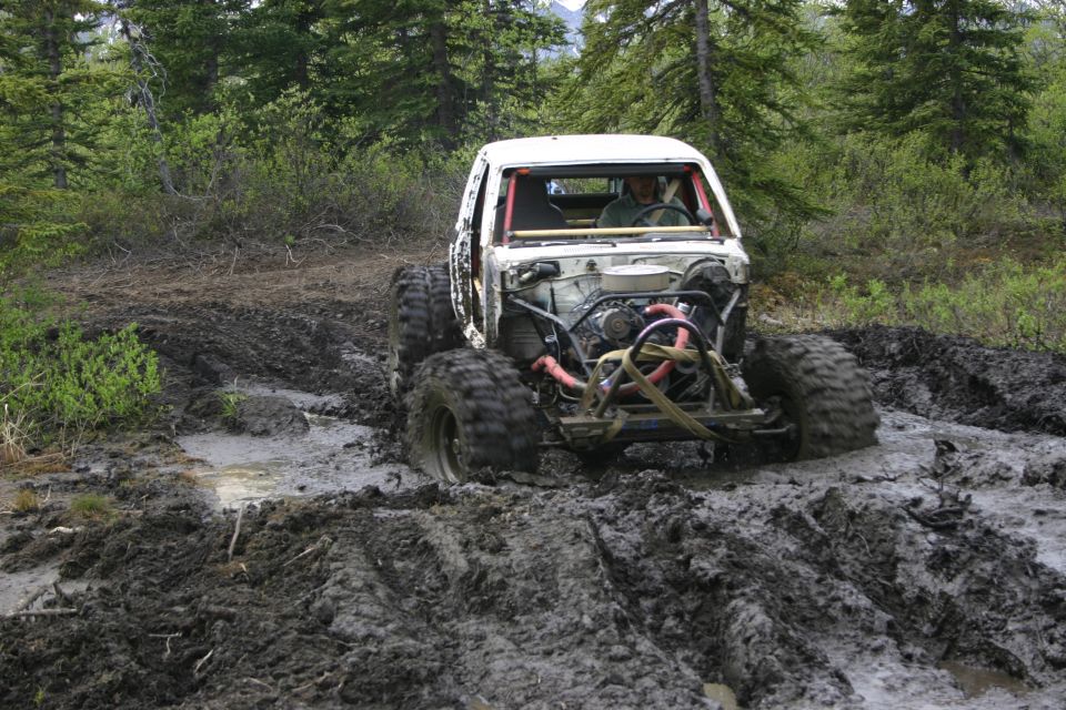 Modified off-road vehicle with exposed engine stuck in deep mud on a wooded trail