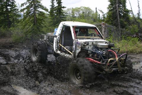 2003 Jeep TJ - Modified truck navigates a muddy trail with large tires kicking up dirt.