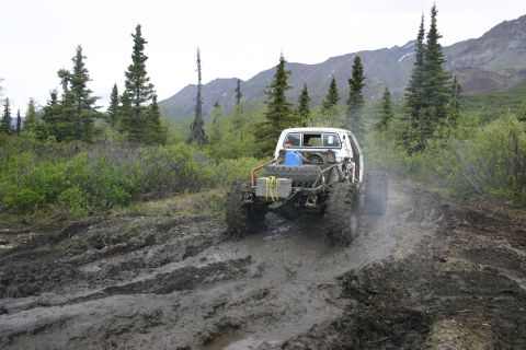 2003 Jeep TJ - An off-road vehicle navigates a muddy trail in a wooded, mountainous area.