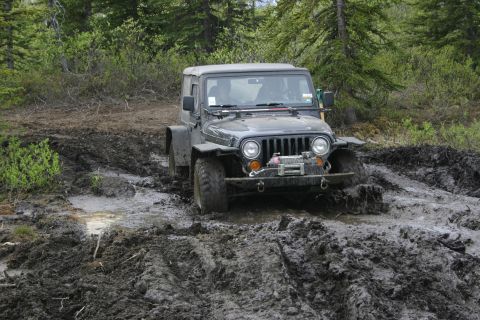 2003 Jeep TJ - A 2003 Jeep TJ struggles through a deep mud pit on a wooded trail.